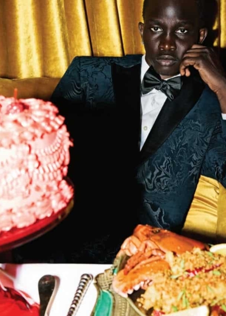 Black male model in a smoking suit behind a feast of food